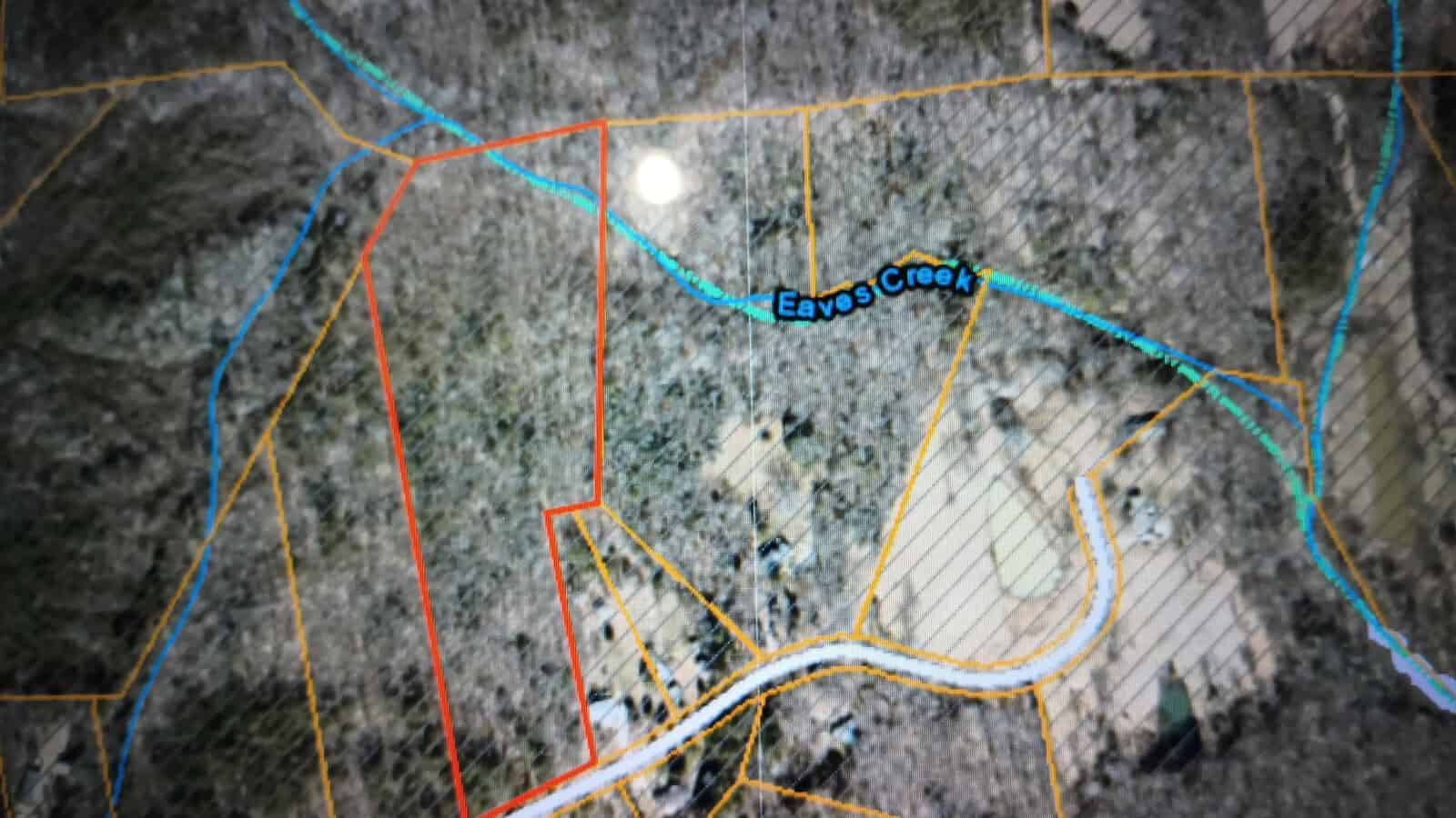 A topographical map showing an outlined red rectangular area adjacent to Eaves Creek. Various colored lines represent boundaries and paths, and the map includes a mix of fields and forested areas. The central portion features marked roads and buildings.