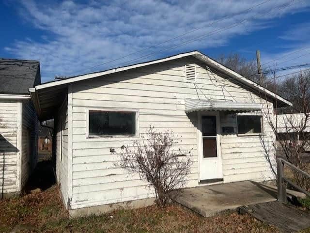 A small, white, single-story house with weathered siding and a front porch under a clear sky.