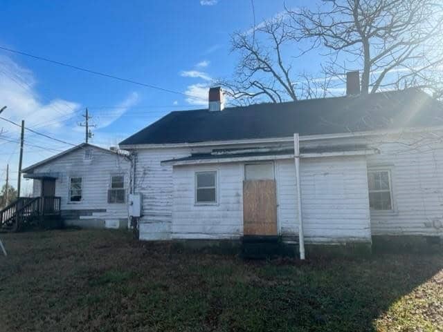 A weathered white house with boarded-up windows under a clear sky.