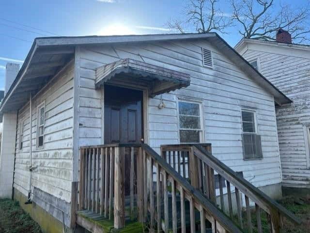 A weathered, white wooden house with a small porch and an aged set of stairs under a clear sky.