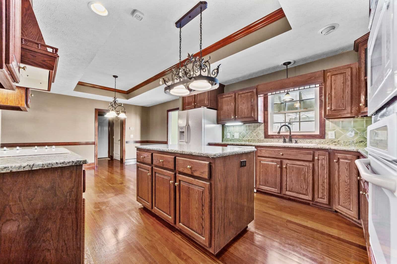 A spacious kitchen interior with cherry wood cabinets, stainless steel appliances, a central island, and hardwood flooring.