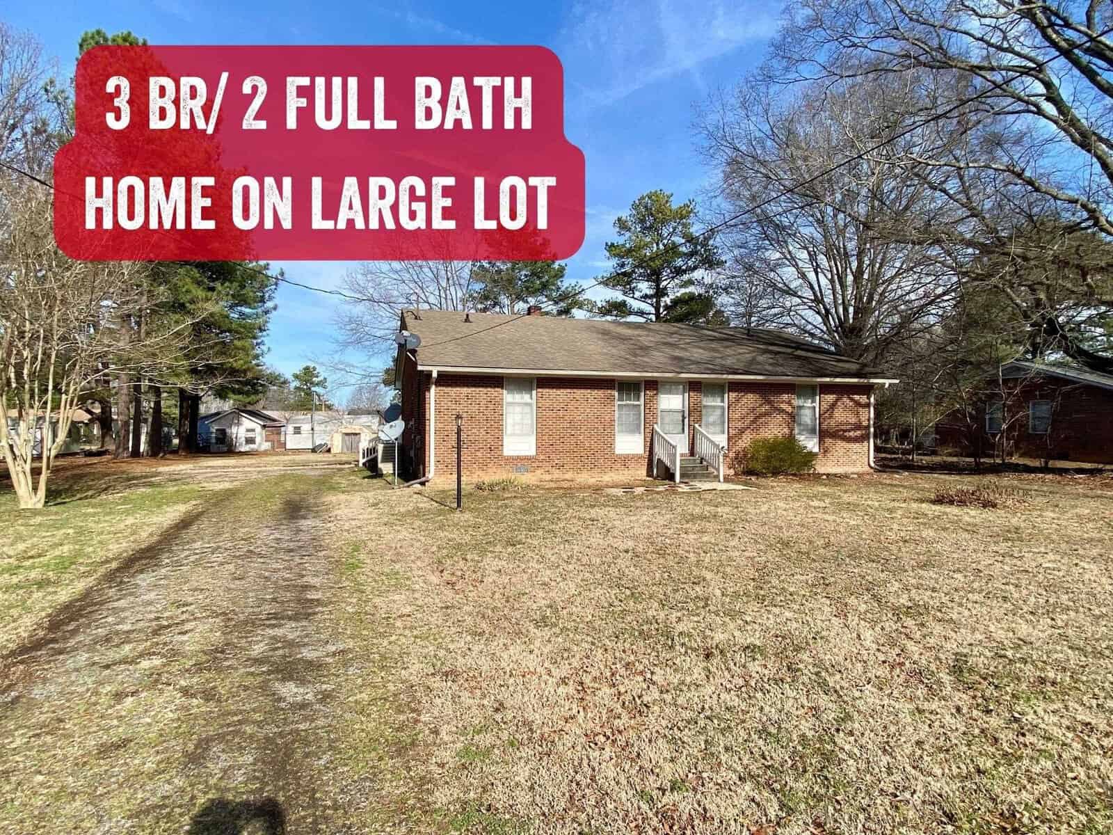 Brick single-story house located at 184 Willow Oak Drive, Henderson NC, with three bedrooms and two full bathrooms situated on a spacious lot with trees and a clear blue sky.