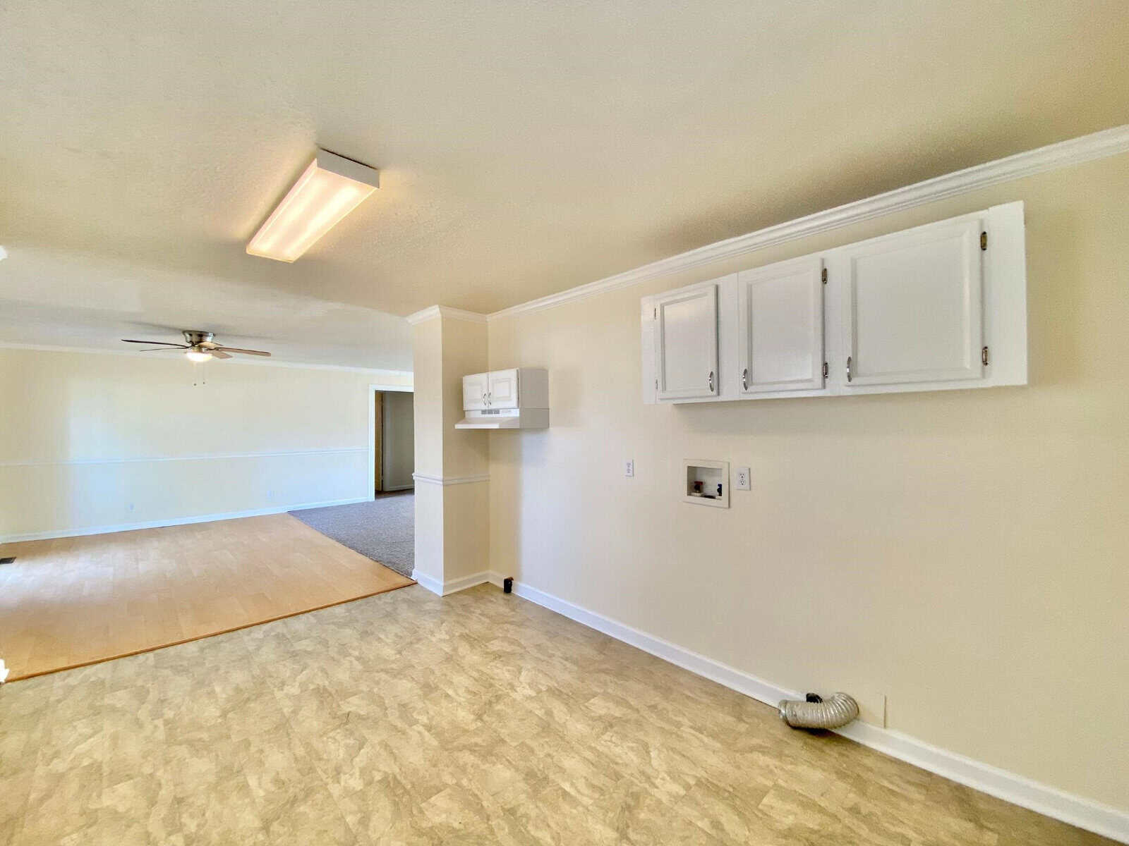 An empty, well-lit room with white walls featuring an attached fan, white cabinetry, and vinyl flooring.