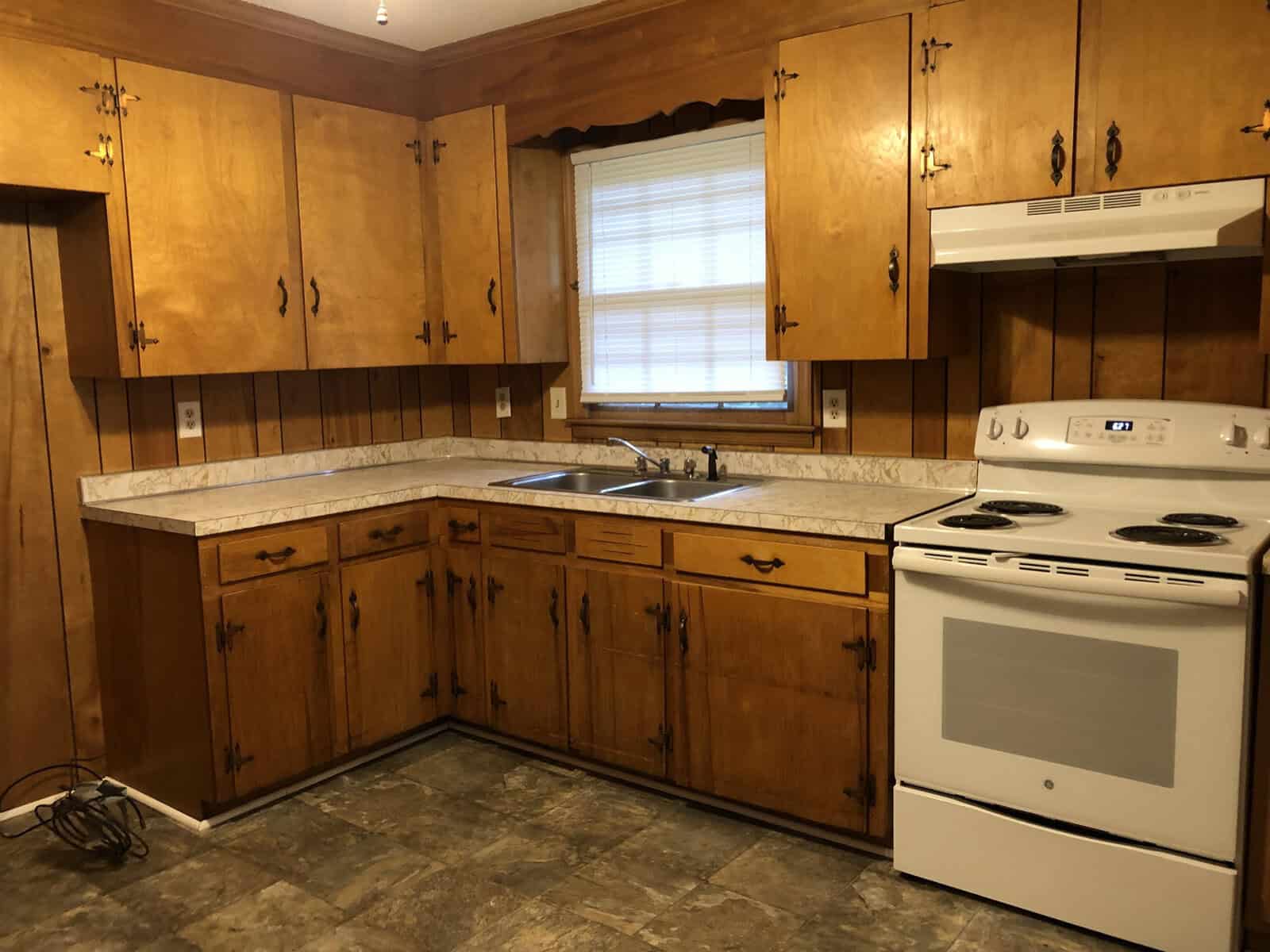 A kitchen with wooden cabinets, laminate countertops, a double sink, and white appliances including a stove.