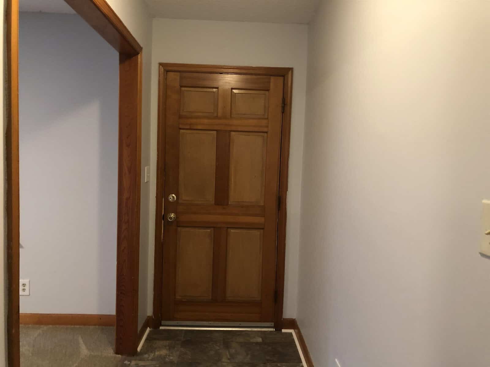 A closed wooden door in a room with beige walls, featuring a visible door frame and light switch to the right.