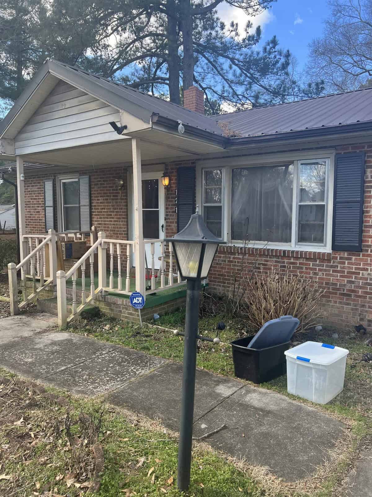 A single-story brick house with a front porch and a street lamp in the yard during the daytime.