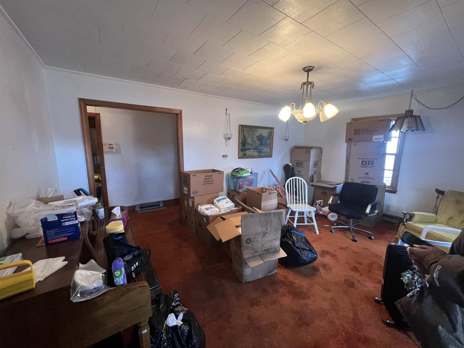 A cluttered room with boxes, packing materials, and various items suggesting a moving or sorting process is underway.