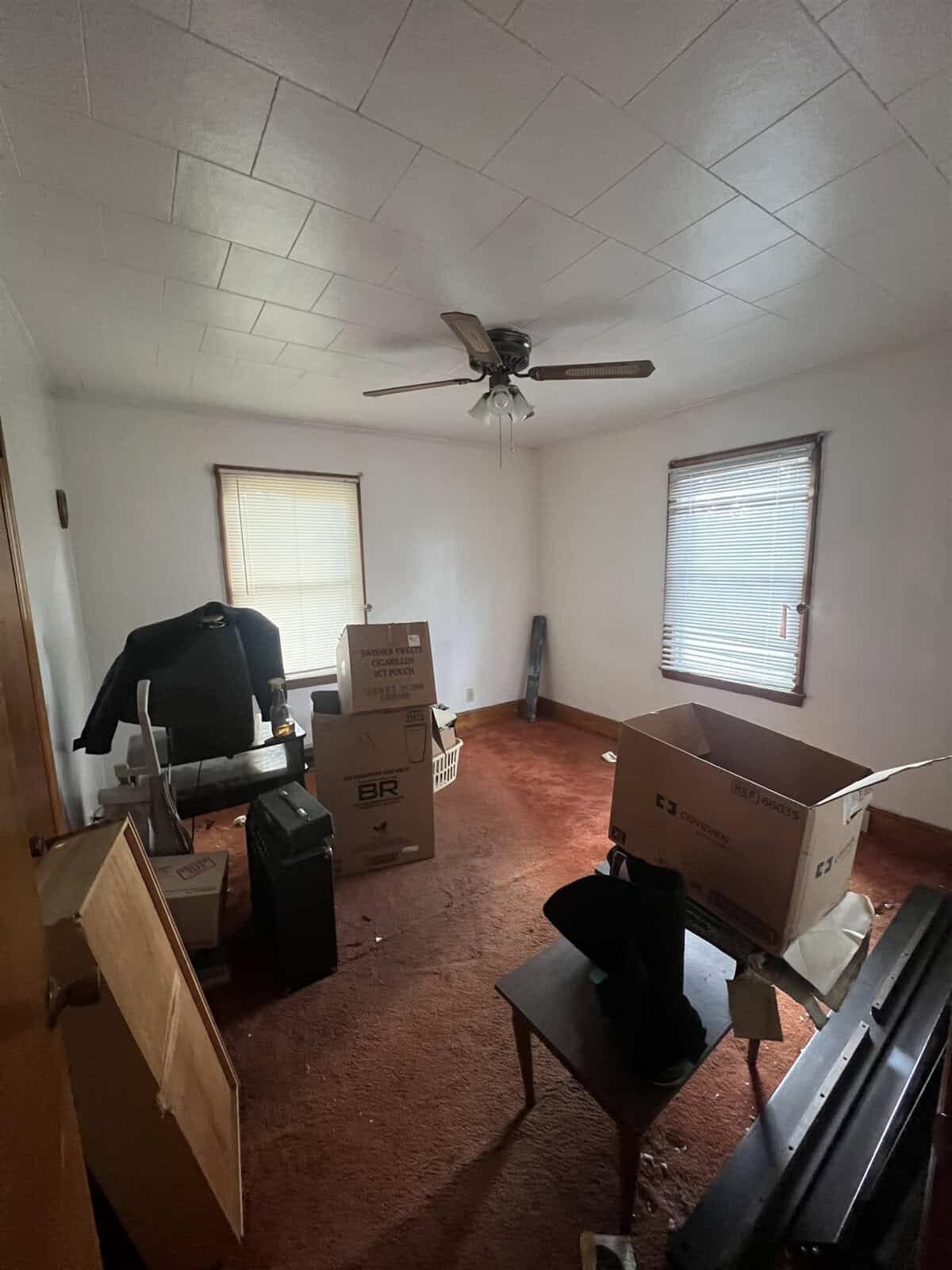 An attic room with a sloped ceiling, showing scattered moving boxes and furniture, and a ceiling fan above.