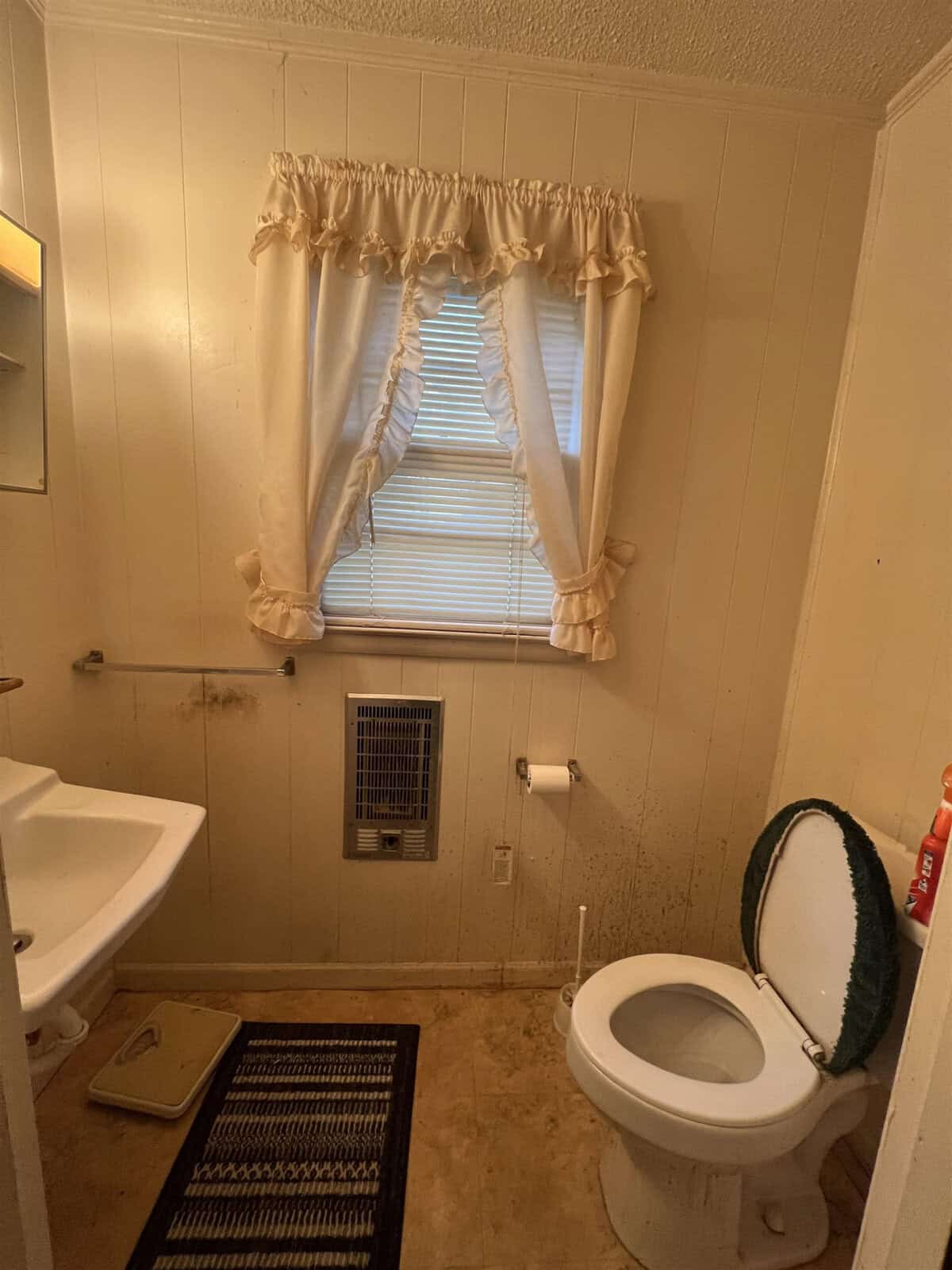 A small bathroom with a toilet, sink, and frilly window curtain.