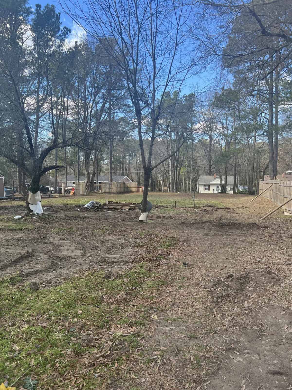 A partially cleared lot with scattered trees, showing early stages of construction or landscaping in a residential area.
