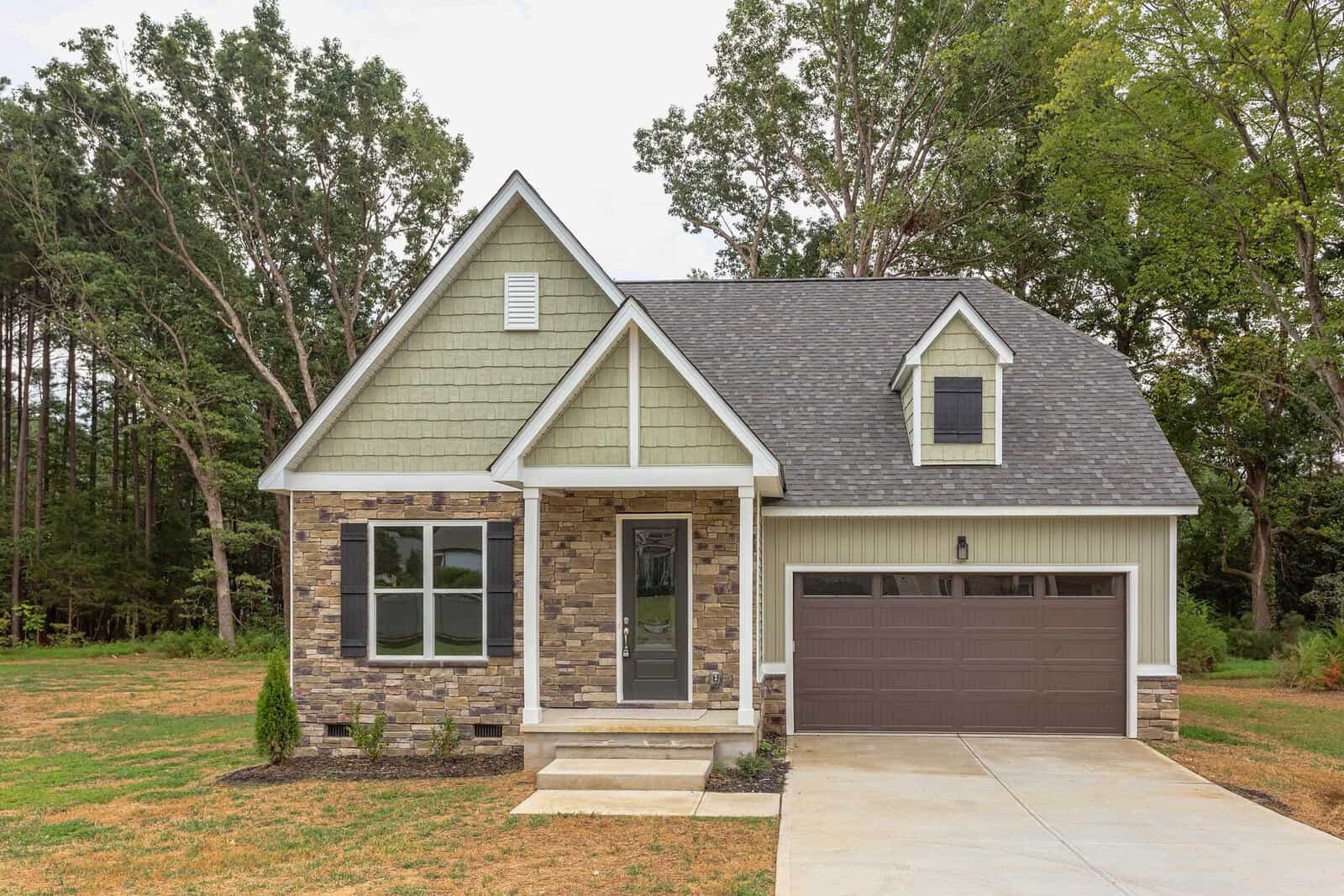 Located at 4506 Gresham Drive, Oxford, this modern suburban house boasts a blend of stone and green siding, a gabled roof, and a two-car garage. The front yard features a neatly manicured lawn with a concrete driveway leading to the garage and is framed by tall trees in the background.