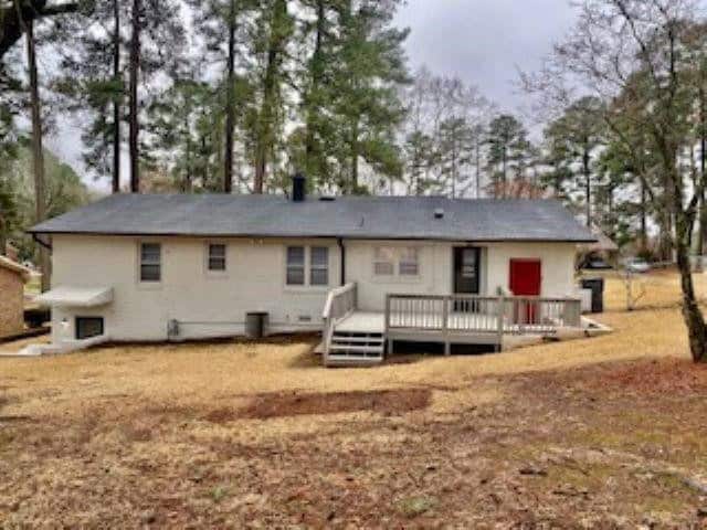 A single-story house with white siding and a red door, featuring a small deck at the front, situated in a yard with scattered trees and a blanket of fallen leaves.