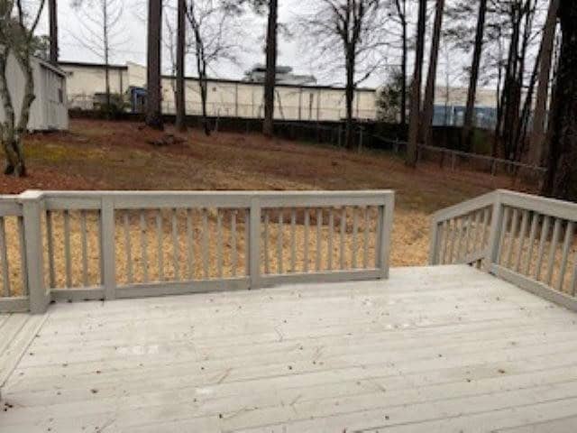 Wooden deck overlooking a backyard with a view of a mobile home and trees in the distance.