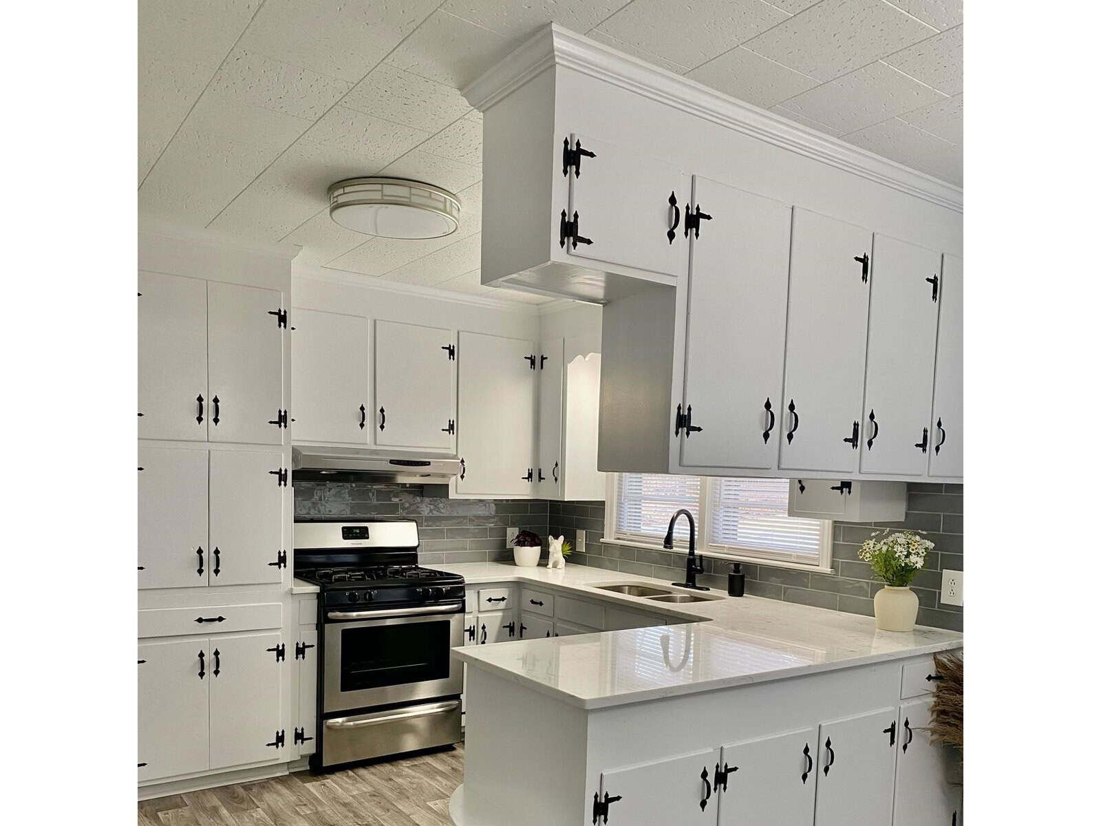 A modern kitchen with white cabinetry, black hardware, stainless steel appliances, and a white countertop.