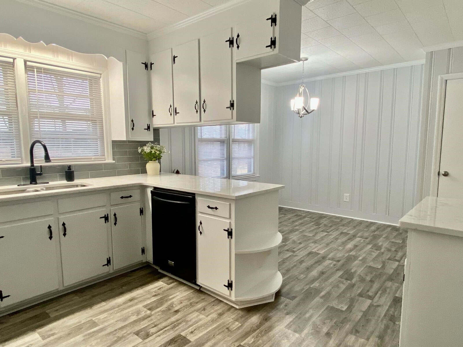 A modern kitchen featuring white cabinetry with black hardware, light gray wood-look flooring, and a chandelier above the sink area.