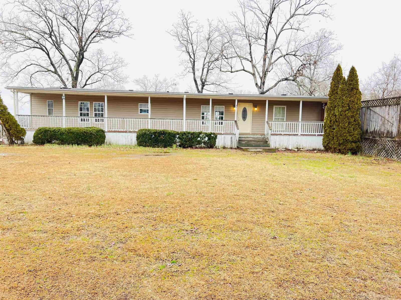 The single-story beige house at 40 N Plummer Avenue in Middleburg features a charming wraparound porch set against leafless trees. Brown grass covers the yard, and a small staircase leads to the front door, flanked by two tall bushes, adding to its quaint appeal.