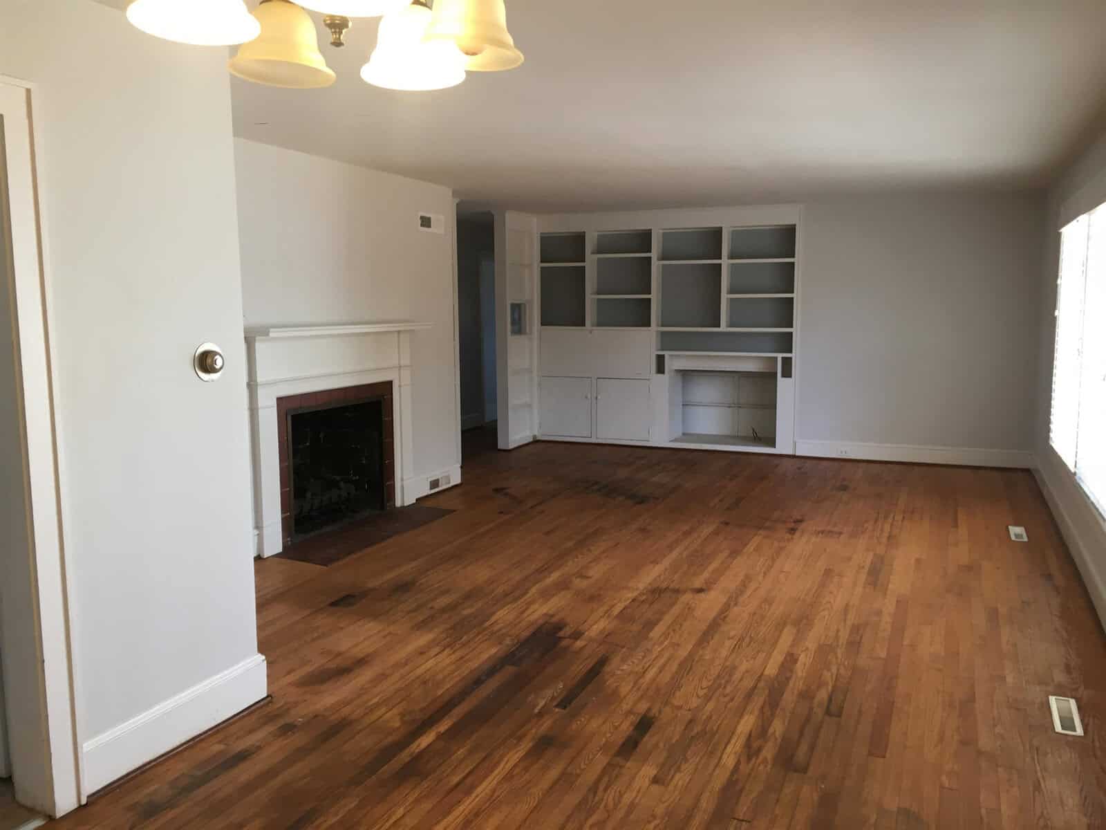 An empty room with hardwood flooring, a white fireplace on the left, and built-in shelves and cabinets on the right.