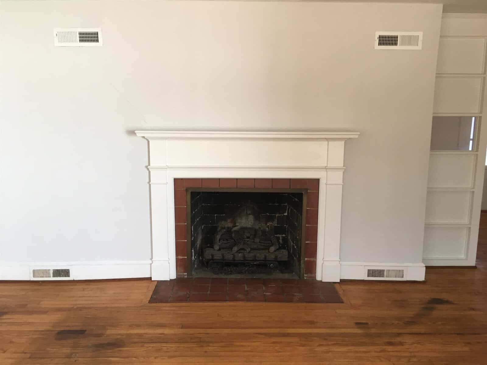 An empty room with polished wooden flooring featuring a white fireplace and built-in shelves on the right-hand side.