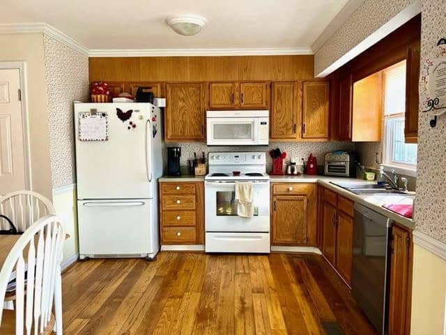 A well-lit, tidy kitchen with wooden cabinets, white appliances, and hardwood flooring.