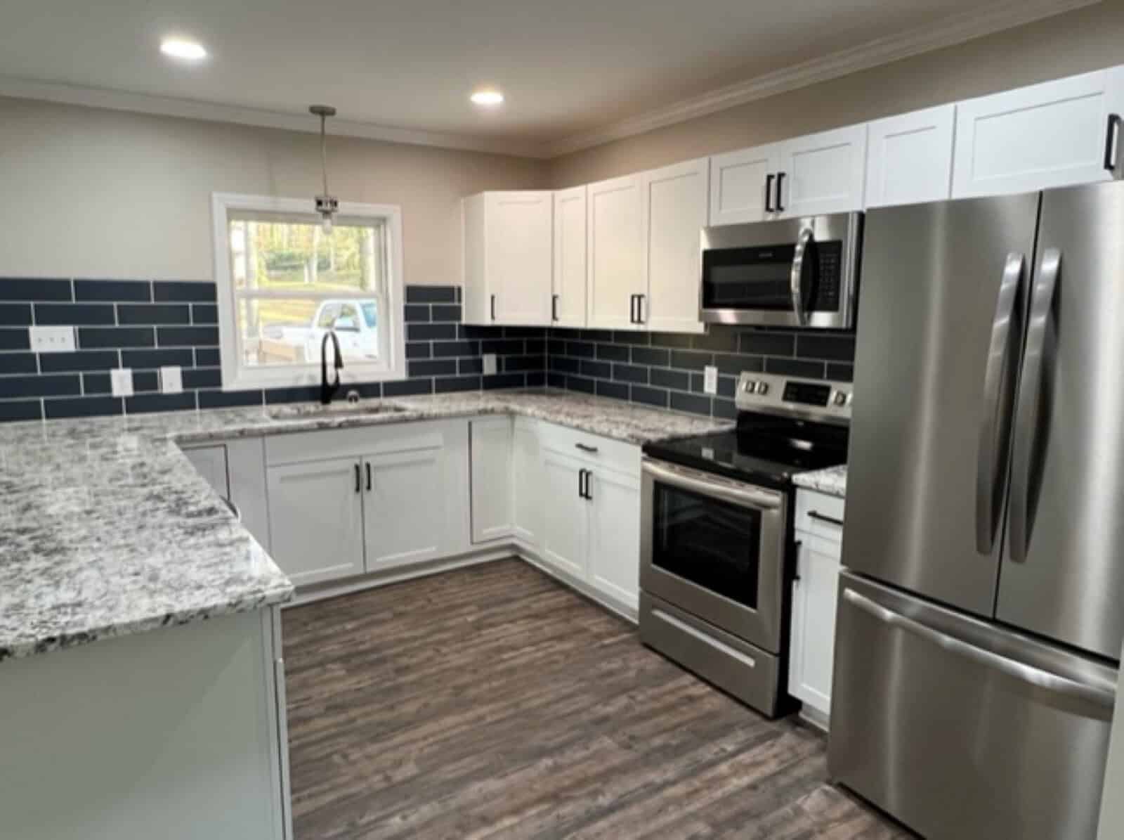 A modern kitchen interior featuring white cabinetry, stainless steel appliances, granite countertops, and a blue subway tile backsplash.