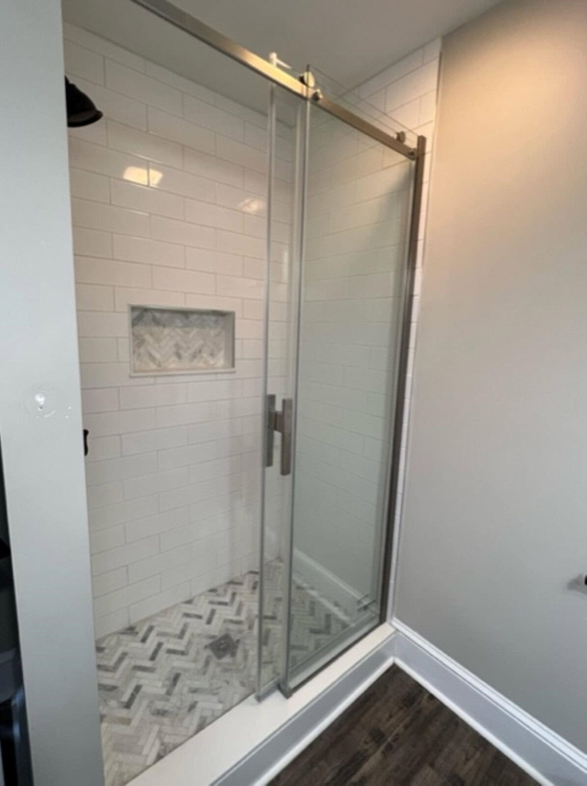 A modern bathroom featuring a glass door shower with white subway tiles and herringbone-patterned floor tiles.