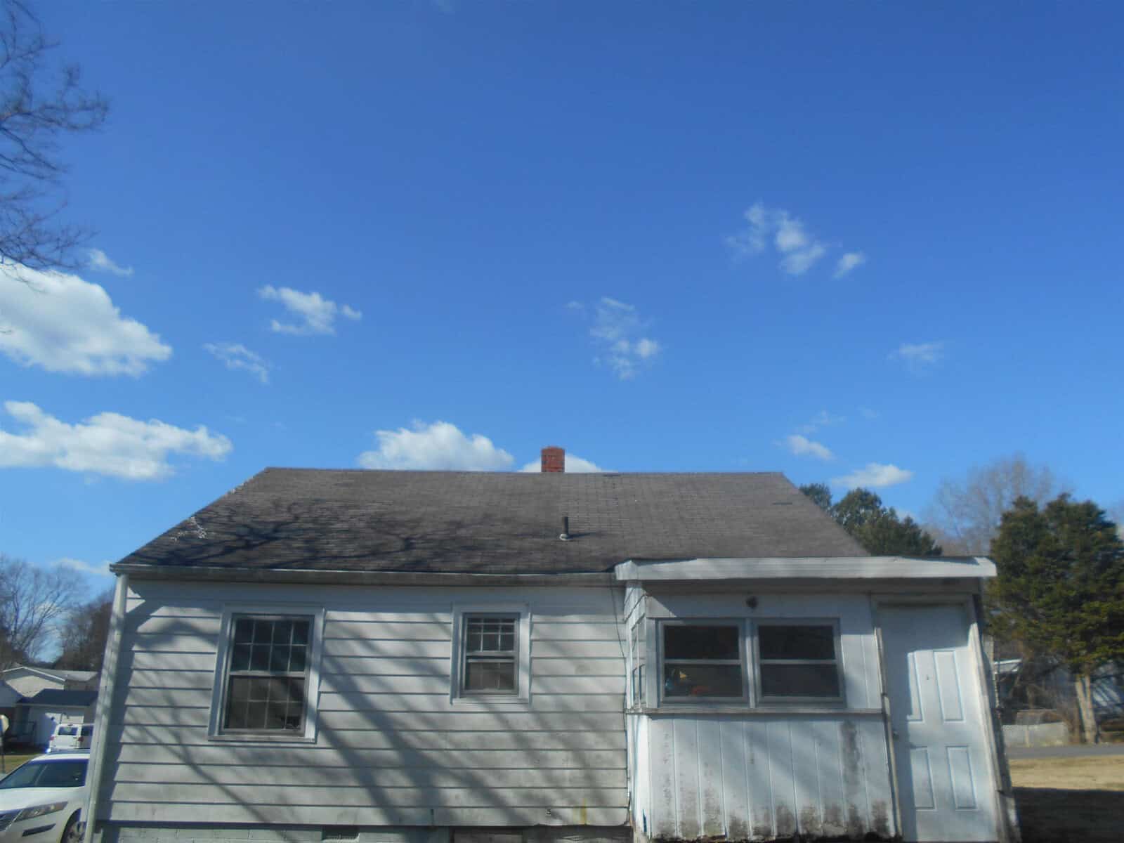 A single-story house with a shingled roof under a blue sky with scattered clouds.