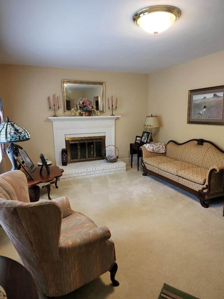 A traditional living room featuring a beige color scheme with a fireplace, a vintage sofa, an armchair, and various decorative items, including a telescope and wall paintings.