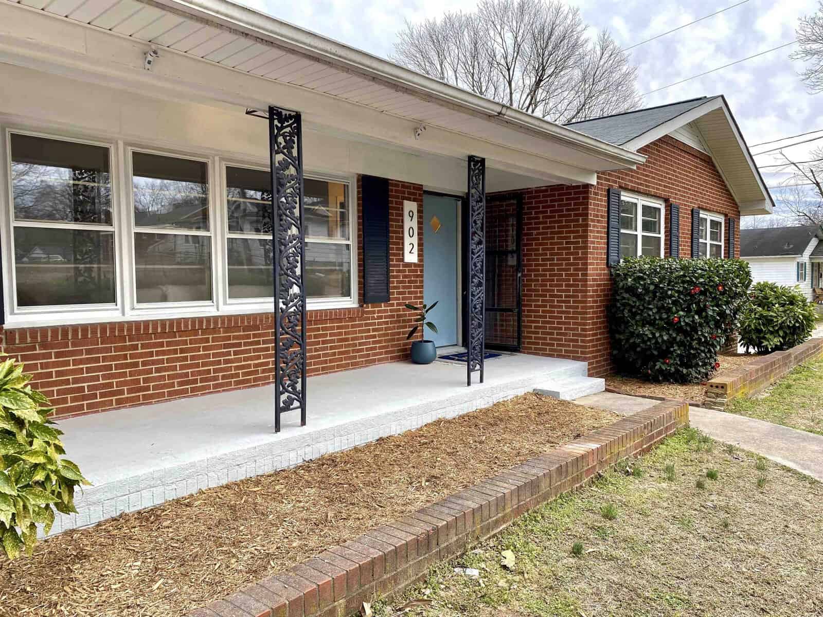A brick house with a covered porch, supported by decorative columns, and a blue front door.