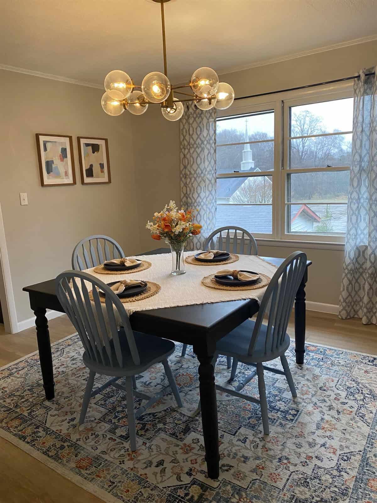 A well-appointed dining area with a four-seater table set for a meal, featuring a modern chandelier above and framed artwork on the wall.