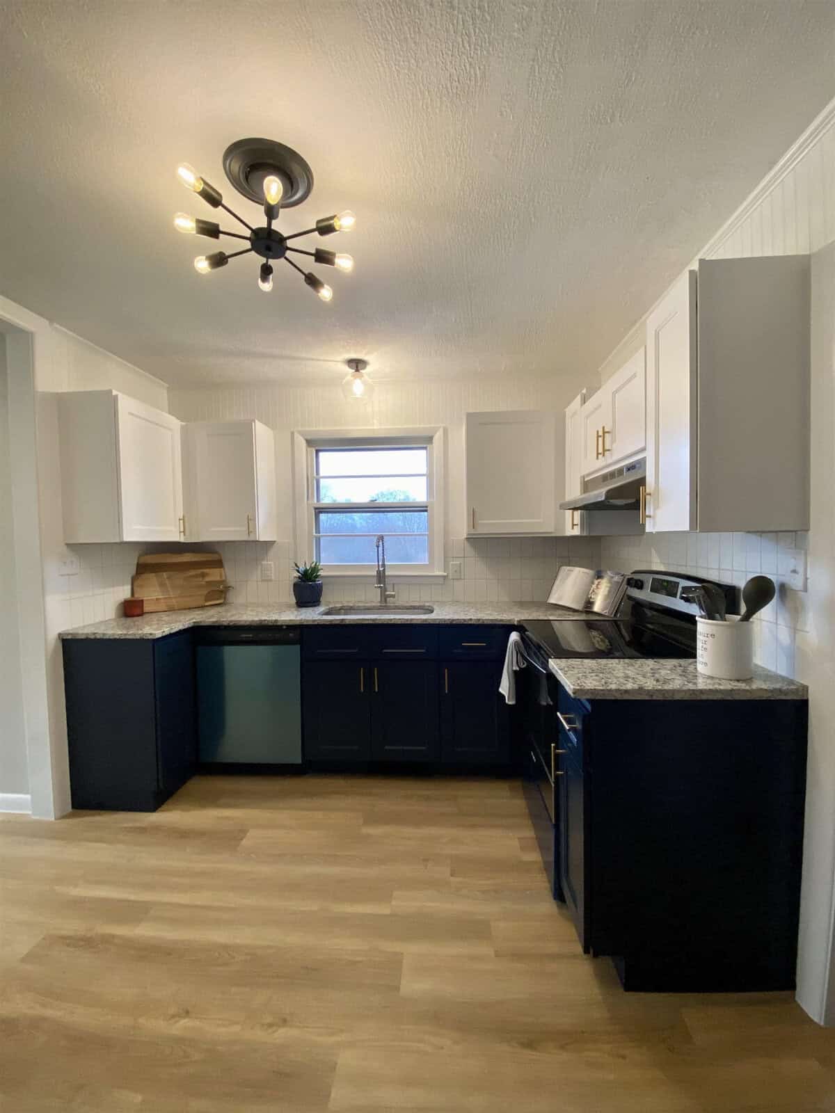 A modern kitchen with white upper cabinets, navy blue lower cabinets, stainless steel appliances, and a wooden floor.