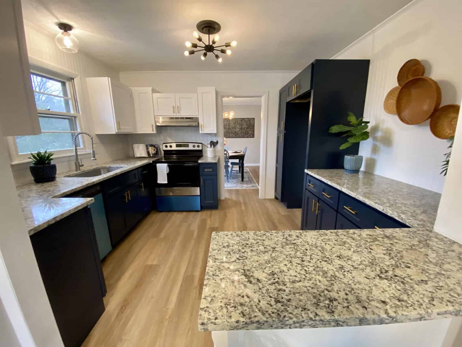 A modern kitchen interior with white cabinetry, dark blue lower cabinets, granite countertops, stainless steel appliances, and hardwood flooring.