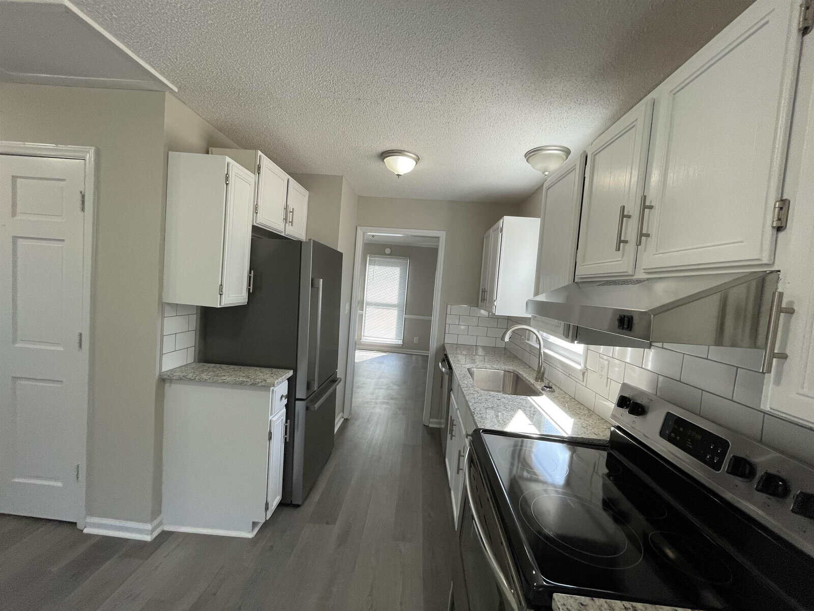 A modern kitchen with white cabinetry, stainless steel appliances, and subway tile backsplash, featuring grey flooring and neutral wall colors.