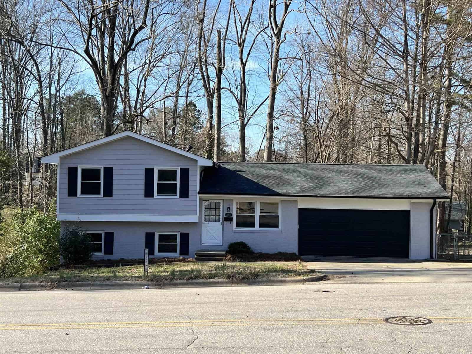 A two-story house with a blue siding and black garage door, situated along a street with leafless trees in the background.