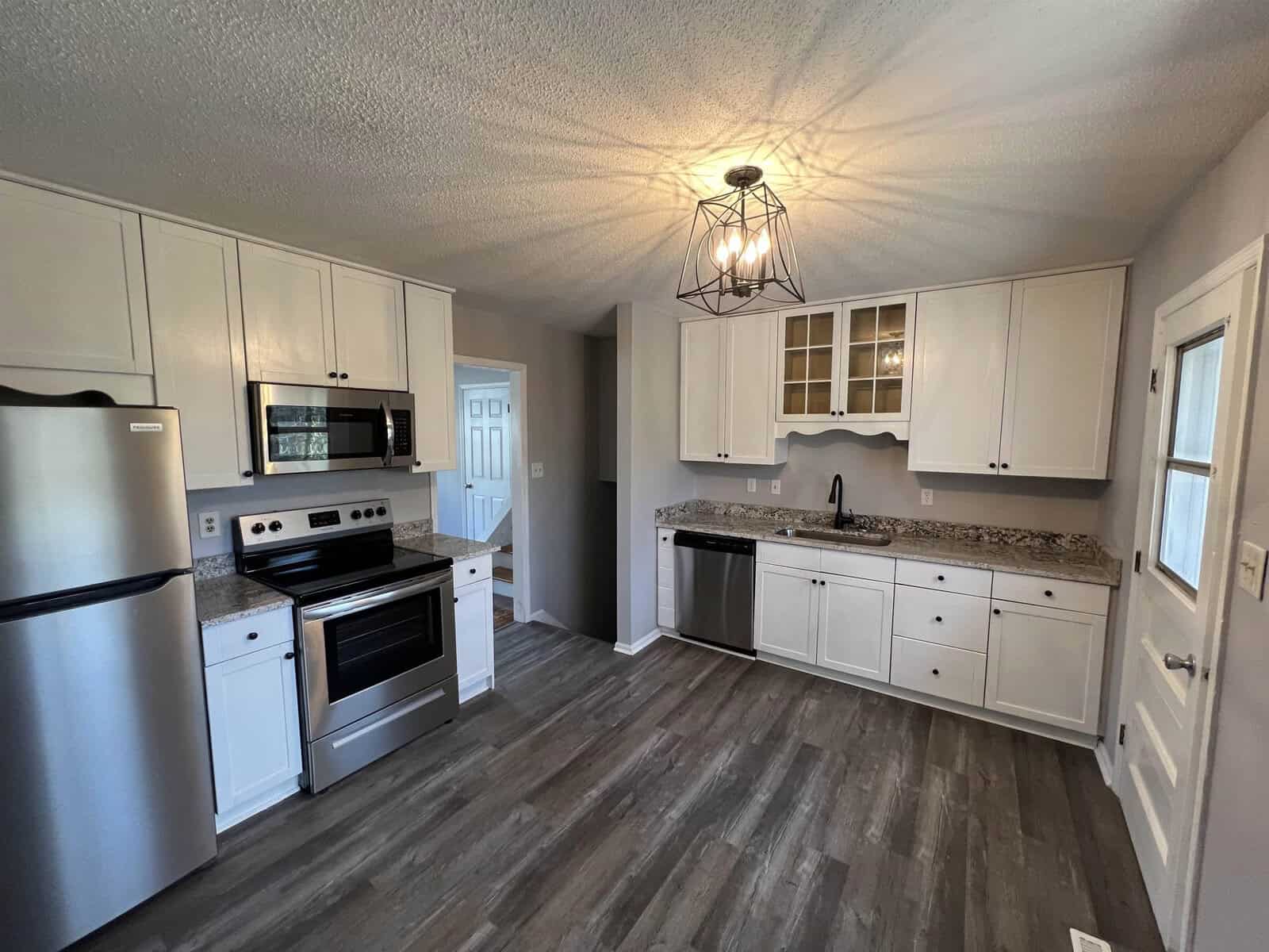 A modern kitchen with stainless steel appliances, white cabinetry, granite countertops, and wood laminate flooring.