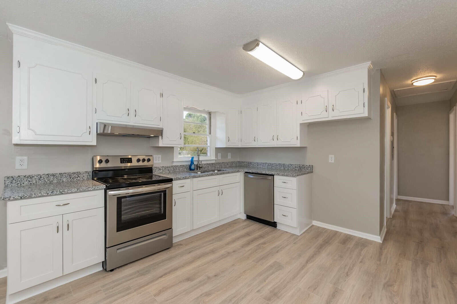 A modern kitchen with white cabinetry, stainless steel appliances, and granite countertops with ample natural light coming through a window.