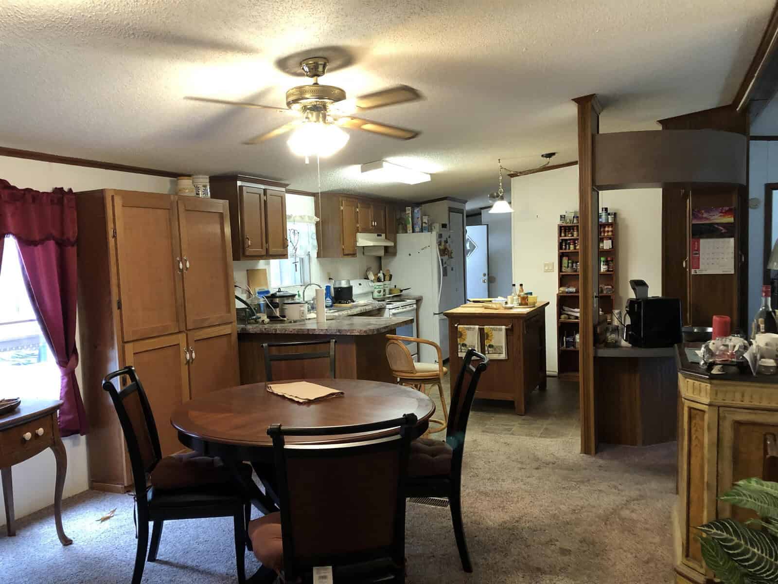 A well-lit, lived-in kitchen and dining area with wooden cabinetry, a dining table set for four, and various household items and appliances visible on the countertops.