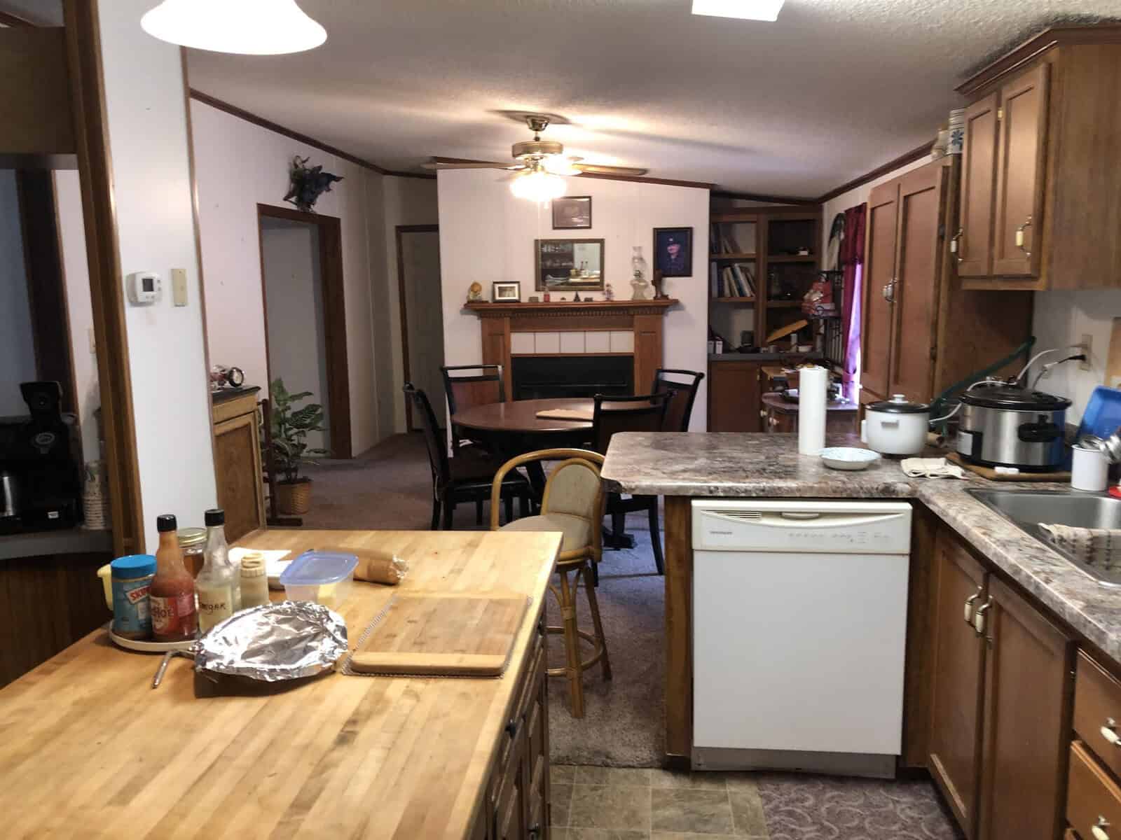 A residential kitchen with wooden cabinets and a dining area in the background, featuring a dishwasher, various kitchen utensils, and some food items on the countertop.
