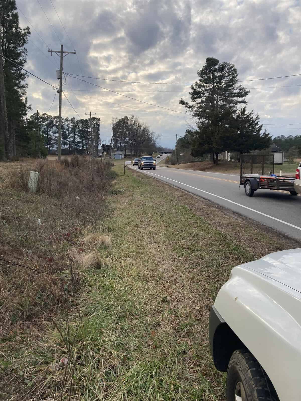 A vehicle parked on the side of a rural road with another vehicle approaching in the distance under a cloudy sky.