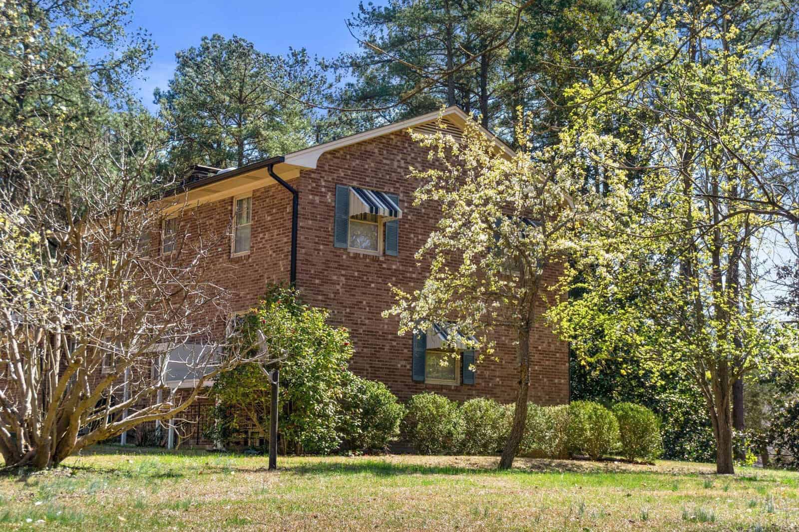 A two-story brick house surrounded by trees and shrubbery on a sunny day.
