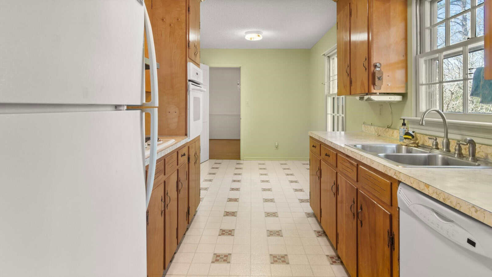 A spacious kitchen with wooden cabinets, white appliances, a double sink, and a tile floor.