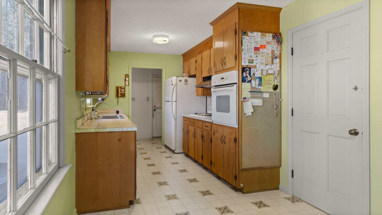 A long, narrow kitchen with wooden cabinets, white appliances, and a linoleum floor.