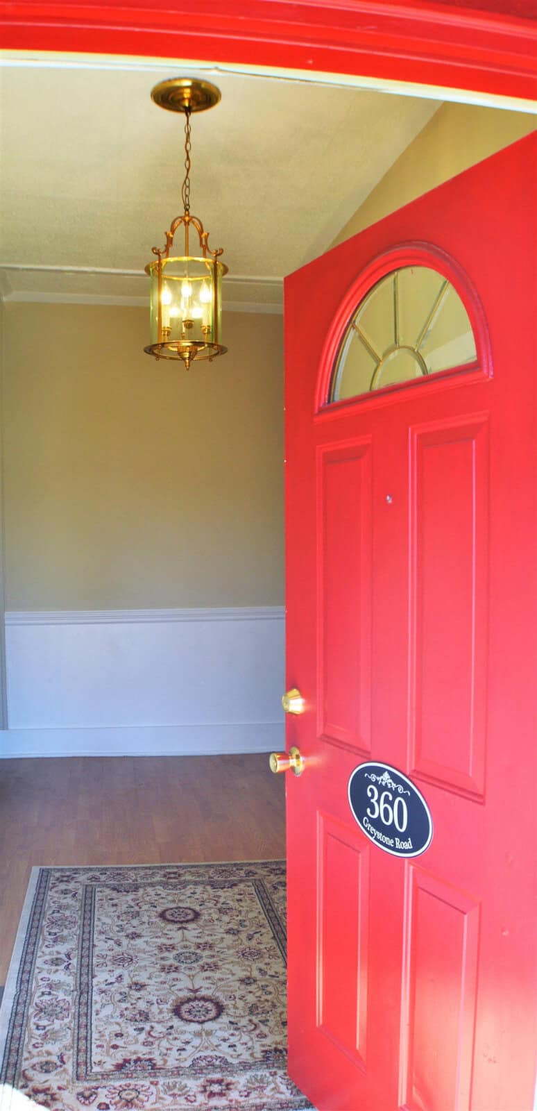 Red front door partially open to a home interior, featuring a hanging light fixture and an ornamental rug in the entryway.
