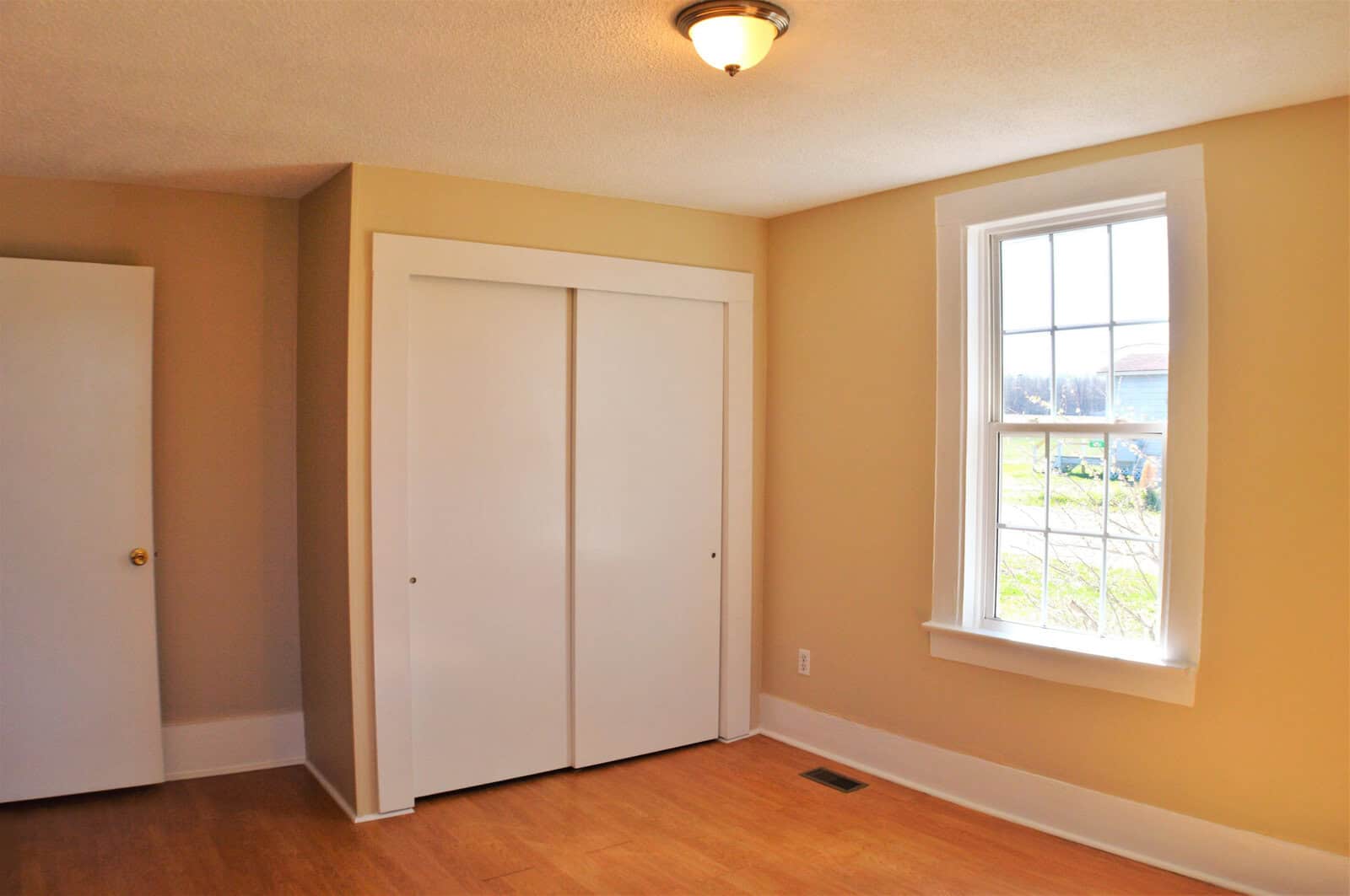 Empty room with a closed white closet, a window providing natural light, and beige walls.