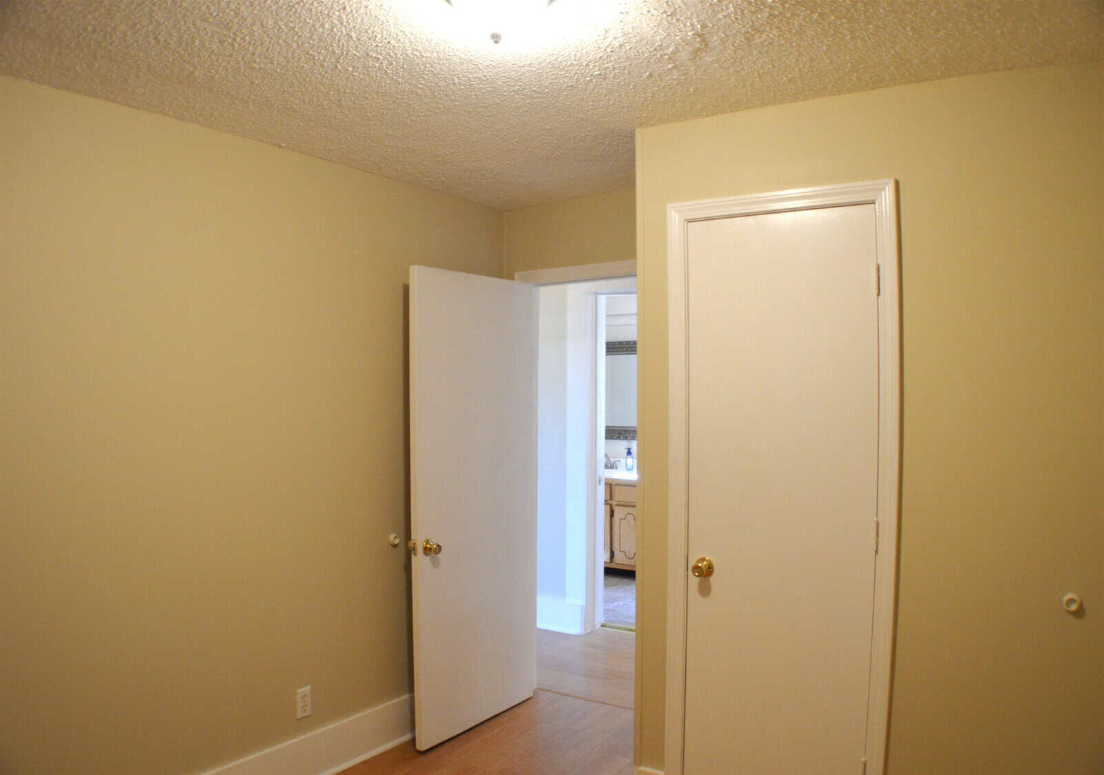 An empty room with beige walls featuring an open door leading to another room and a closed white door on the right.