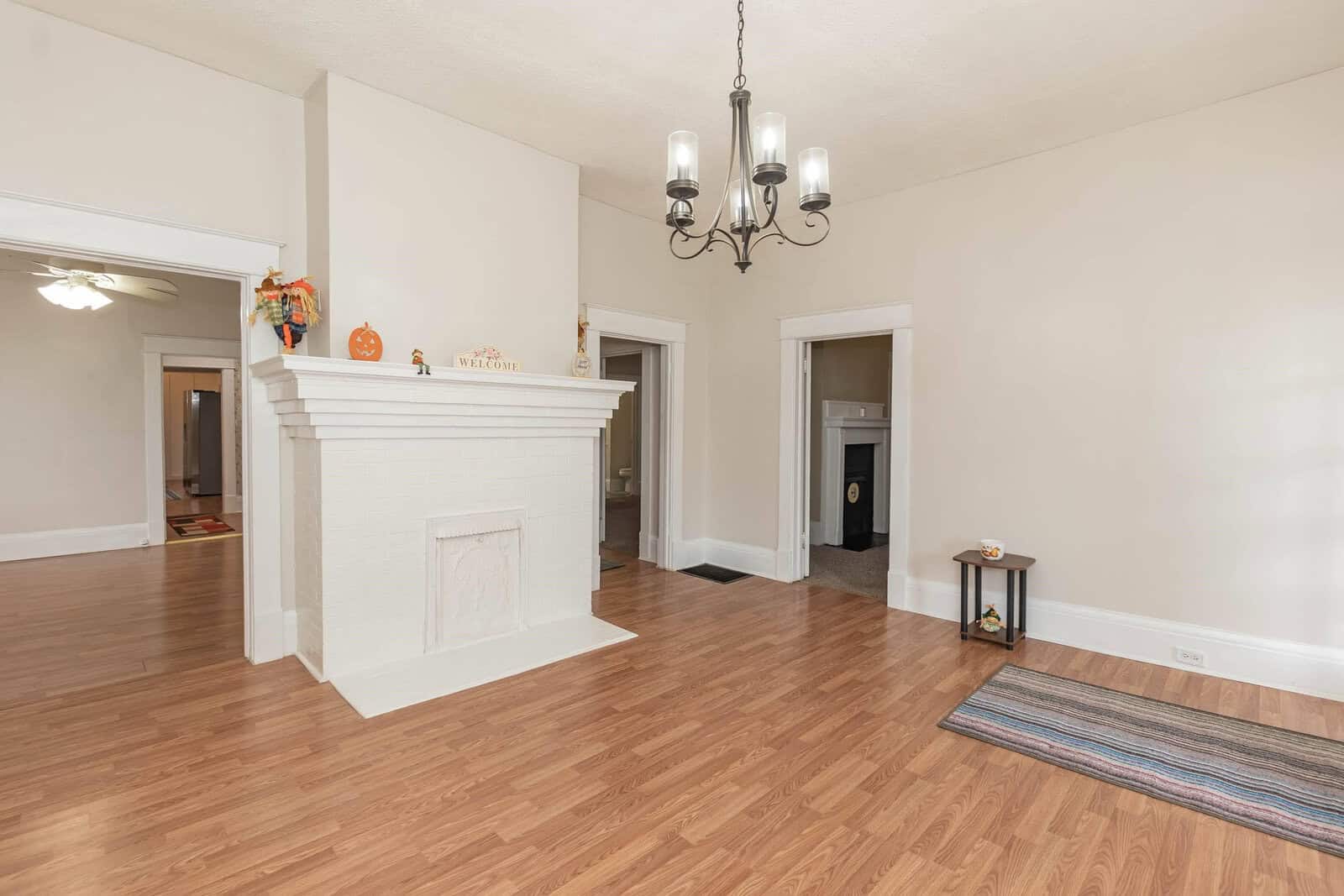 Spacious room with hardwood flooring featuring a white fireplace and a chandelier with minimal furnishings.