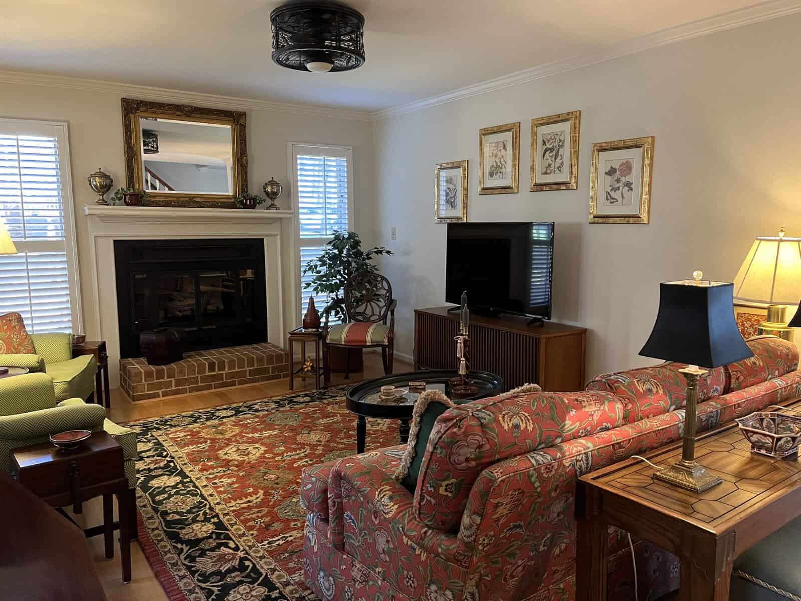 A well-appointed living room featuring a patterned sofa, a brick fireplace, and traditional decor elements including paintings and a persian rug.