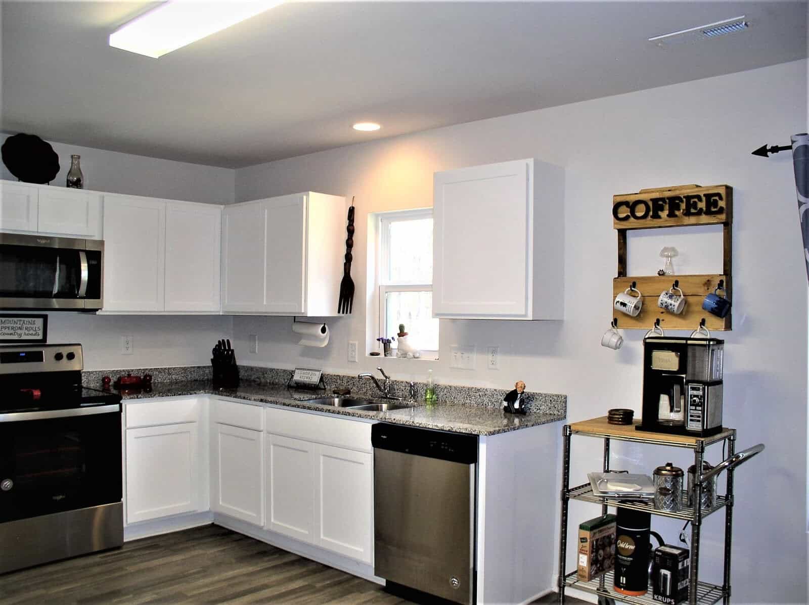 A modern kitchen with white cabinetry, stainless steel appliances, granite countertops, and a small coffee station to the right.