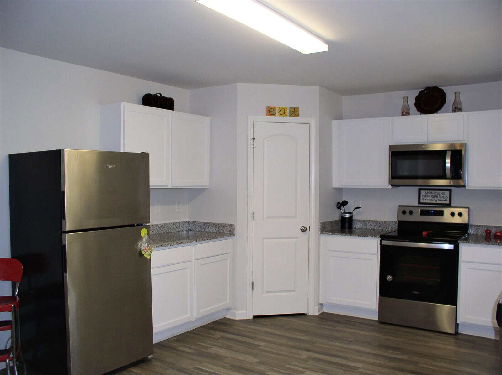 A clean and organized kitchen interior featuring white cabinetry, stainless steel appliances, and grey flooring.