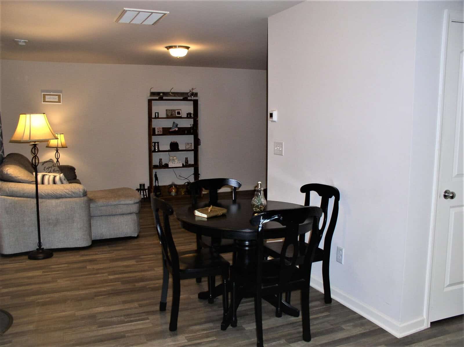 A neatly organized living space featuring a gray sofa, a black dining table with chairs, a lamp, and a shelf with various decorative items.