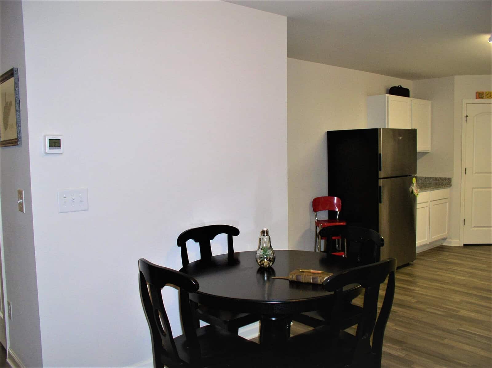 A modern, minimalist dining area with a black table and chairs, adjacent to a kitchen with a refrigerator and white cabinetry.